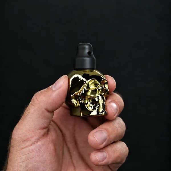 Hand holding a 24 ml skull, gold bottle with a SN*F X-Small sniffer cap